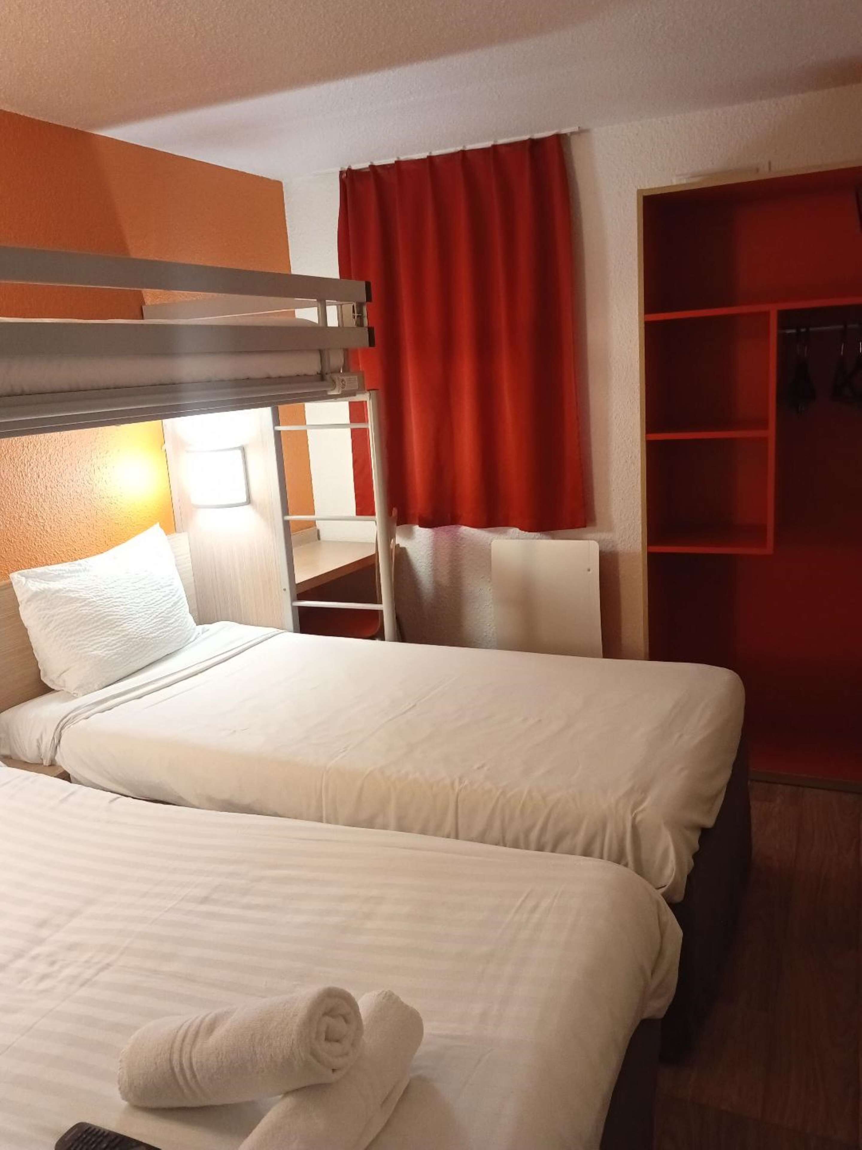 A hotel room with two beds, a bunk bed, a wardrobe, and a mirror.