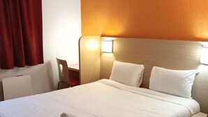 A hotel room with a large bed, white linens, a remote control, and a neatly folded towel on the bed. - Premiere Classe Saint Brice Sous Forêt (Saint-Brice-sous-Foret)