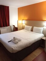 Quarto de hotel com cama grande, roupa de cama branca, controle remoto e toalha dobrada na cama.