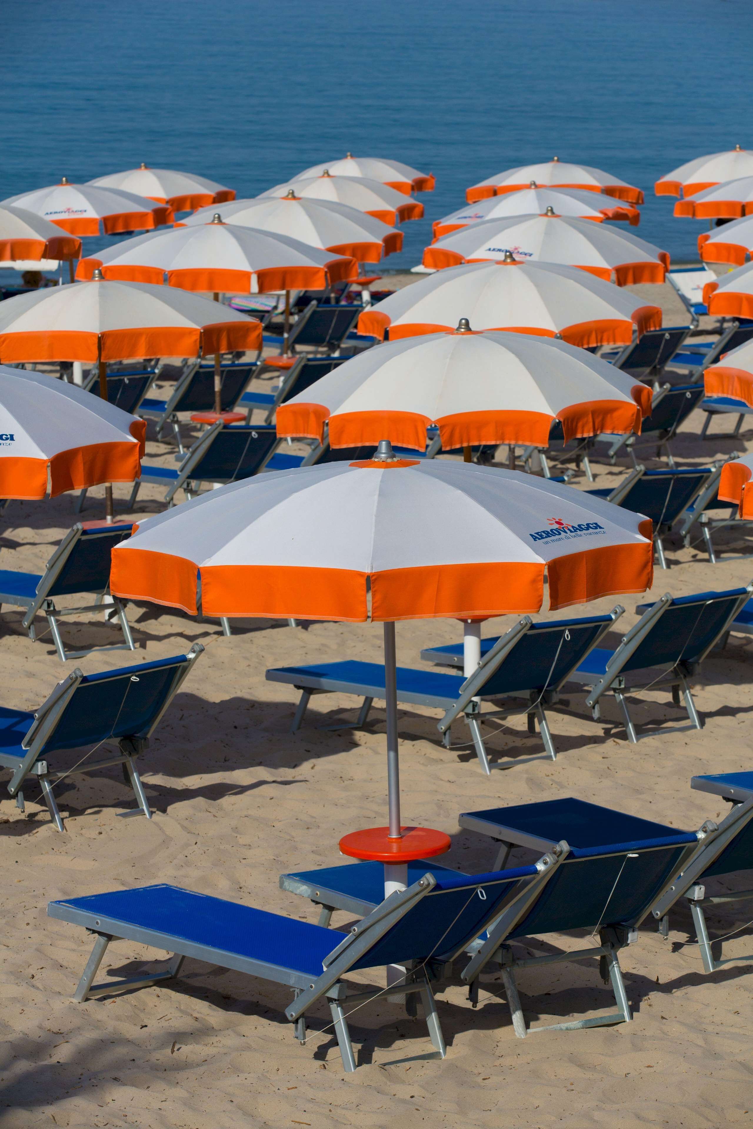 A beach with rows of blue and orange sun loungers and umbrellas.