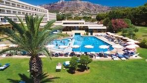 A hotel with a swimming pool surrounded by sun loungers and umbrellas, a palm tree, and a mountainous backdrop. - MClub Lipari (Sciacca)