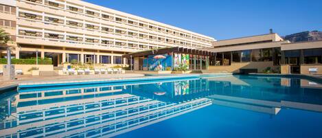Un hotel con una piscina grande, varios pisos y un mural en la pared exterior.