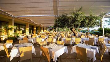 Restaurante al aire libre con varias mesas y sillas de mimbre, cubierto por una marquesina.