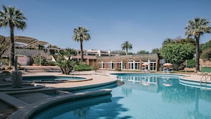 Una piscina con varios niveles y palmeras, rodeada de edificios y zonas de estar al aire libre.