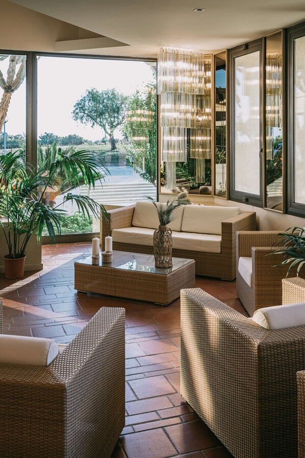 Una sala de estar moderna con muebles de mimbre, una mesa de centro de vidrio y vista a una calle arbolada.