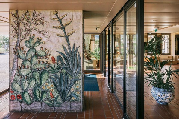 Un vestíbulo con un gran mural de cactus, una puerta de cristal que da a una zona de estar y una planta en maceta en el suelo.