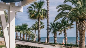 Un área de estar al aire libre con sillas de mimbre, una mesa, palmeras y vista al mar.