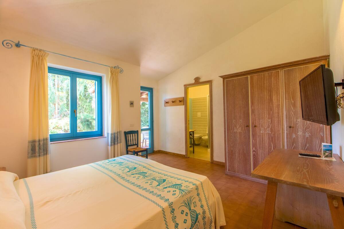 A bedroom with a bed, a wooden desk, a wardrobe, and a window with curtains.