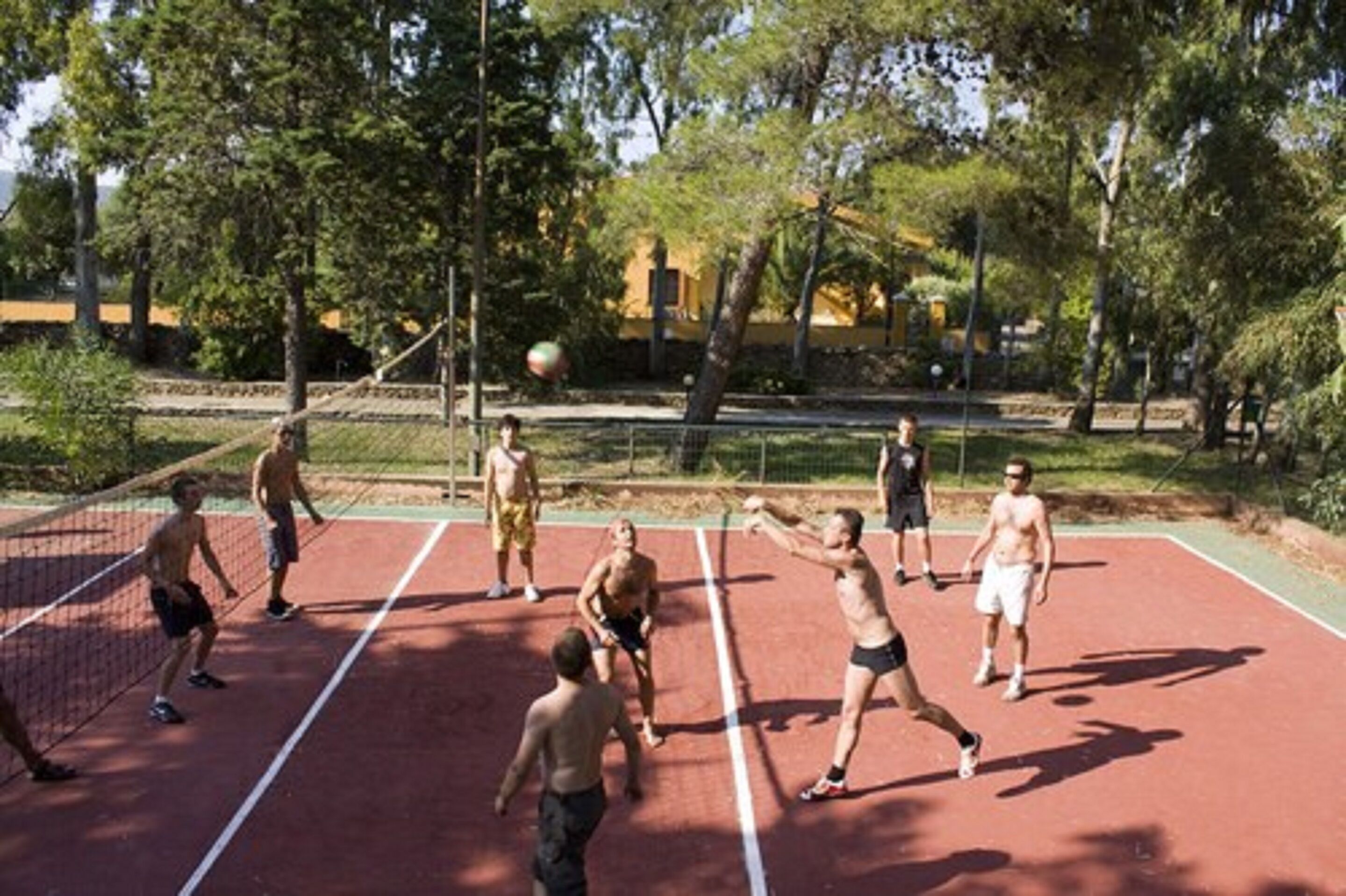 A group of people playing tennis on an outdoor court surrounded by trees.