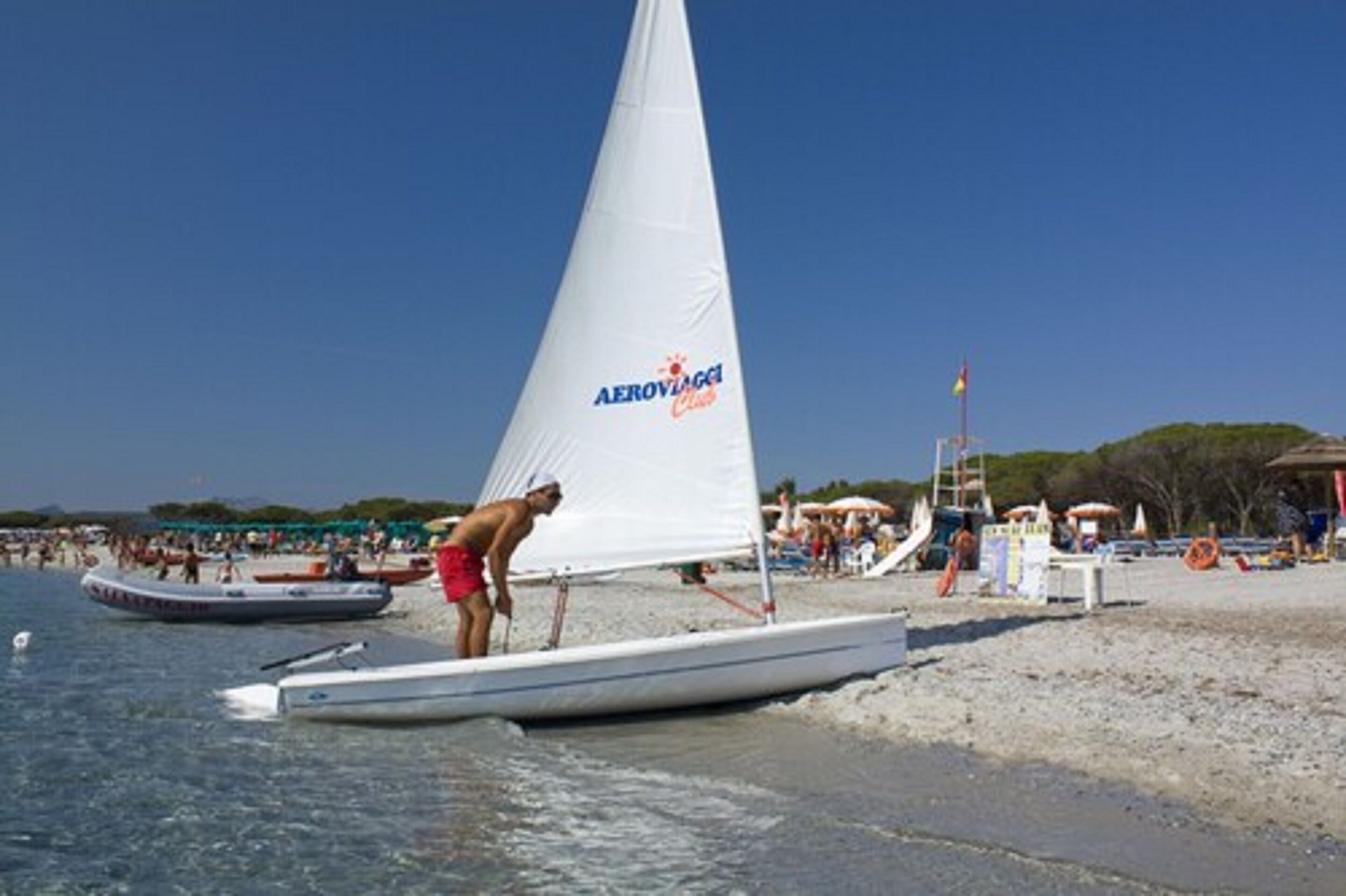 A beach scene with a sailboat named "Aerovaggio Club" and people on the shore.