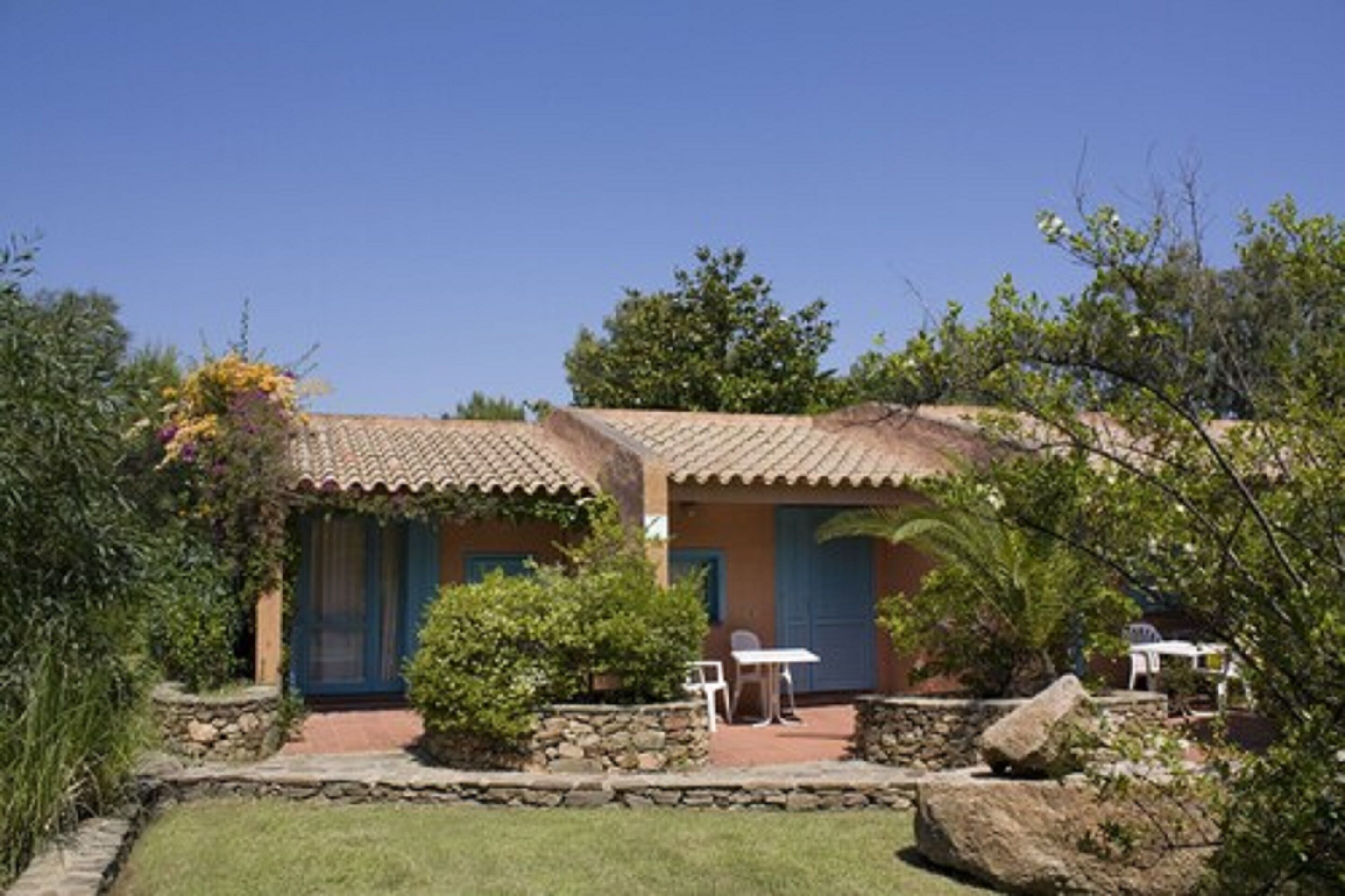 A rustic building with a tiled roof, a stone wall, and a small patio area with a table and chairs.