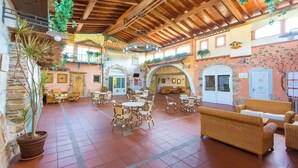 A spacious indoor area with multiple seating arrangements, including wicker chairs and tables, under a high wooden ceiling with exposed beams. - Agrustos Village (Budoni)