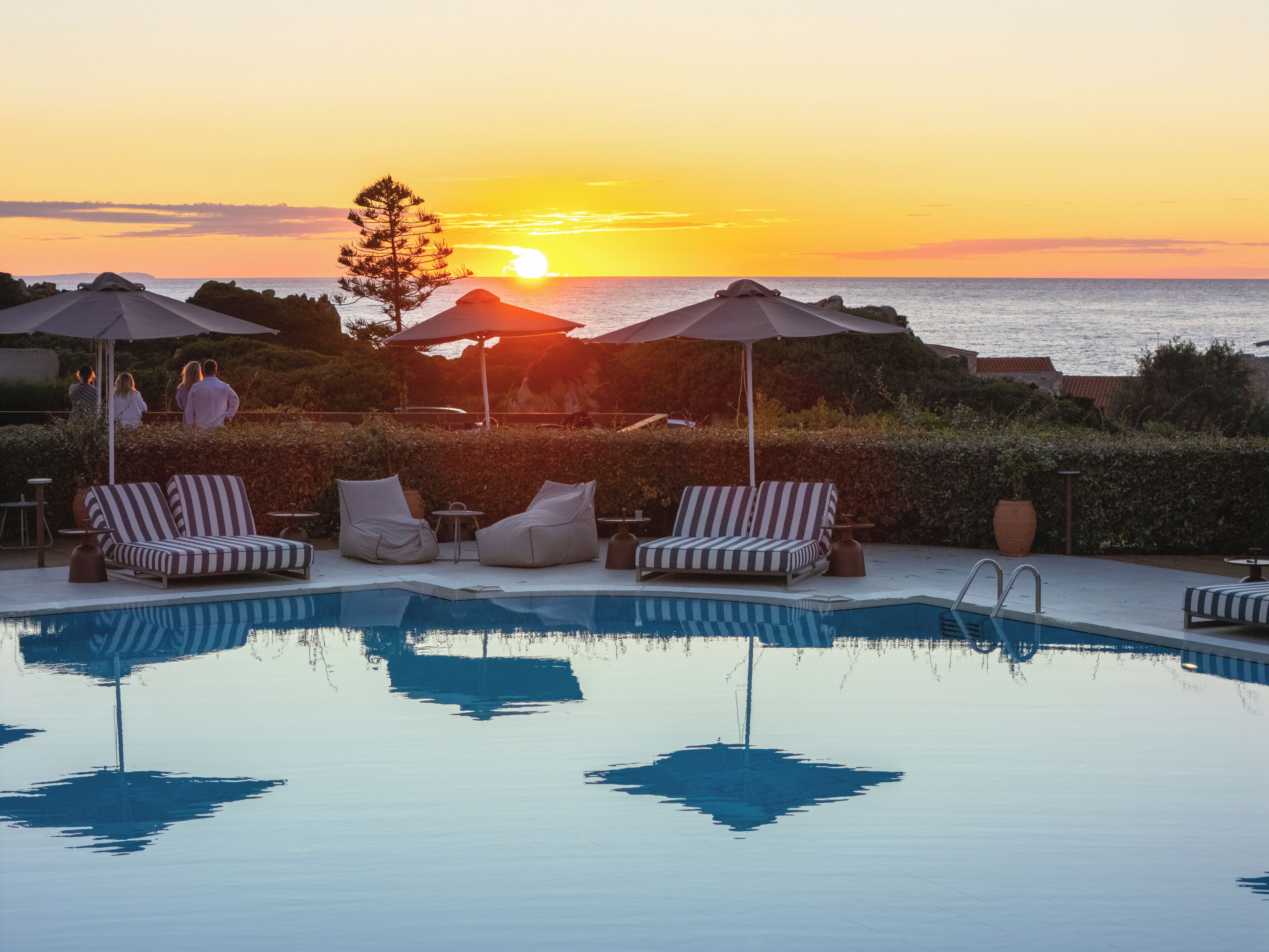 Area piscina con lettini e ombrelloni, vista sul mare al tramonto.