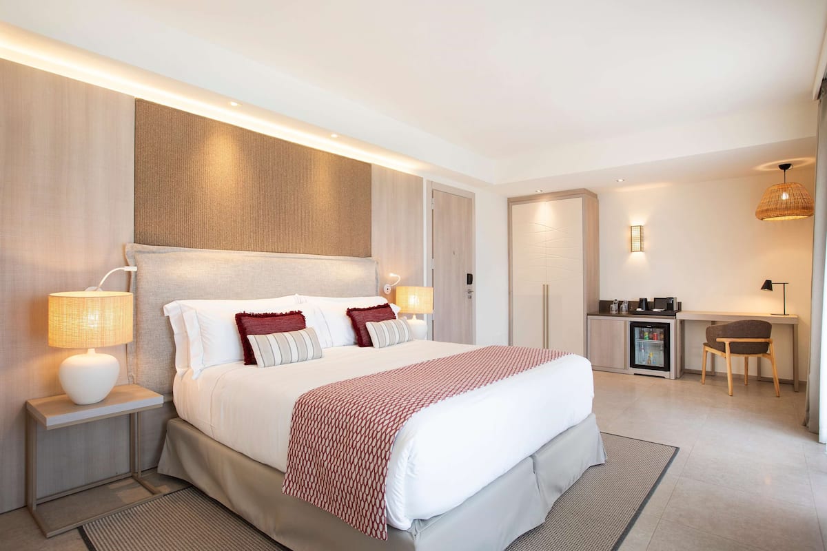 Una habitación de hotel moderna con una cama grande, lámparas de noche, un escritorio y un refrigerador.