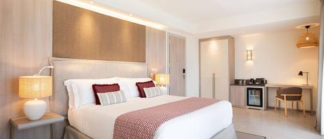 A modern hotel room with a large bed, bedside lamps, a desk, and a refrigerator.