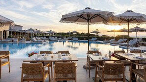 Ein Essbereich am Pool mit Tischen, Stühlen, Sonnenschirmen und Liegestühlen.