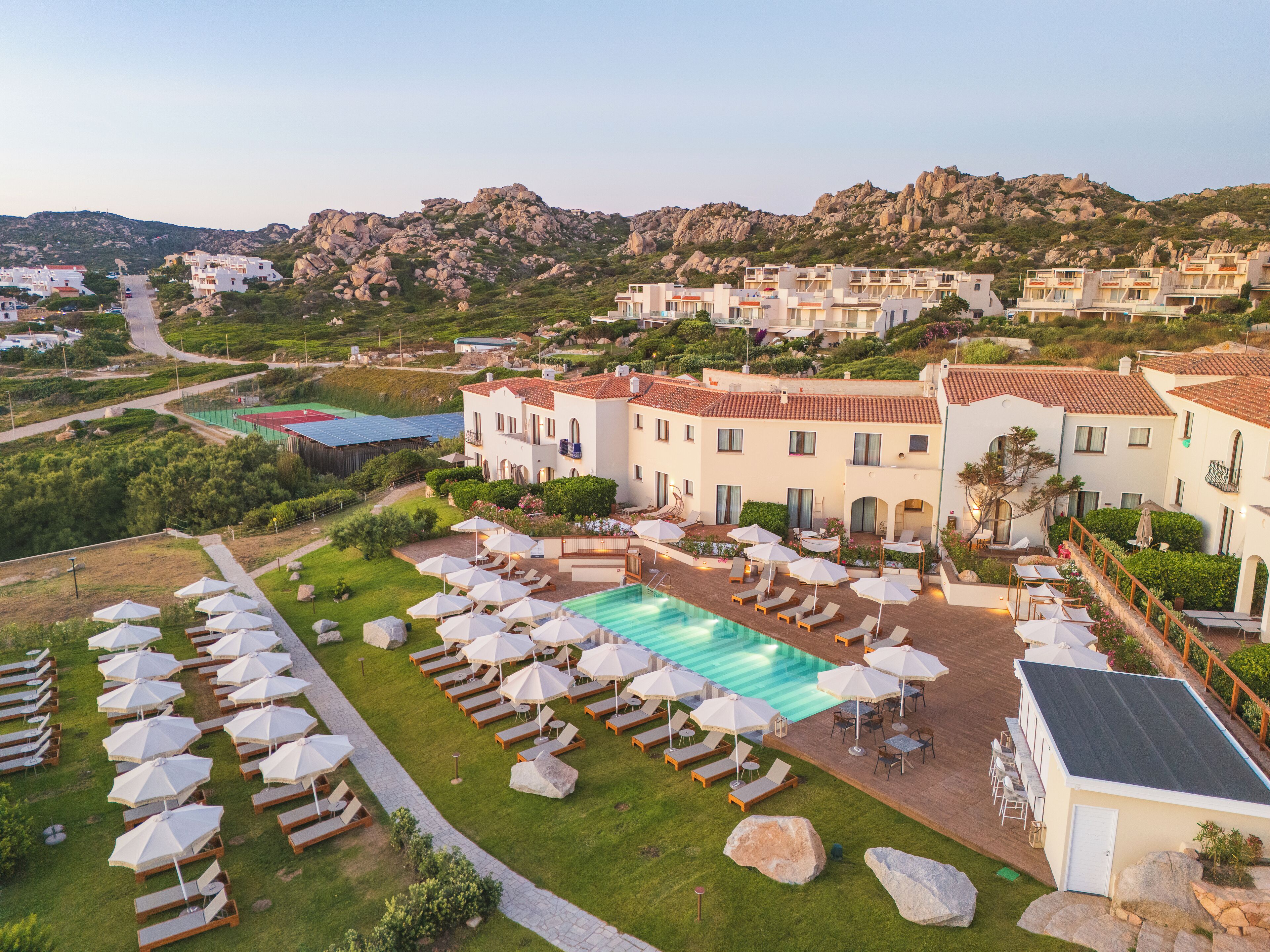 A resort with a swimming pool, sun loungers, and a mountainous backdrop.