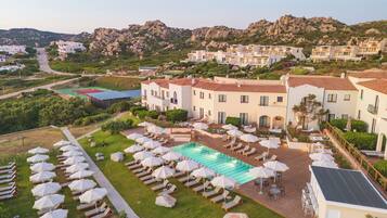 A resort with a swimming pool, sun loungers, and a mountainous backdrop.