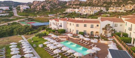 A resort with a swimming pool, sun loungers, and a mountainous backdrop.