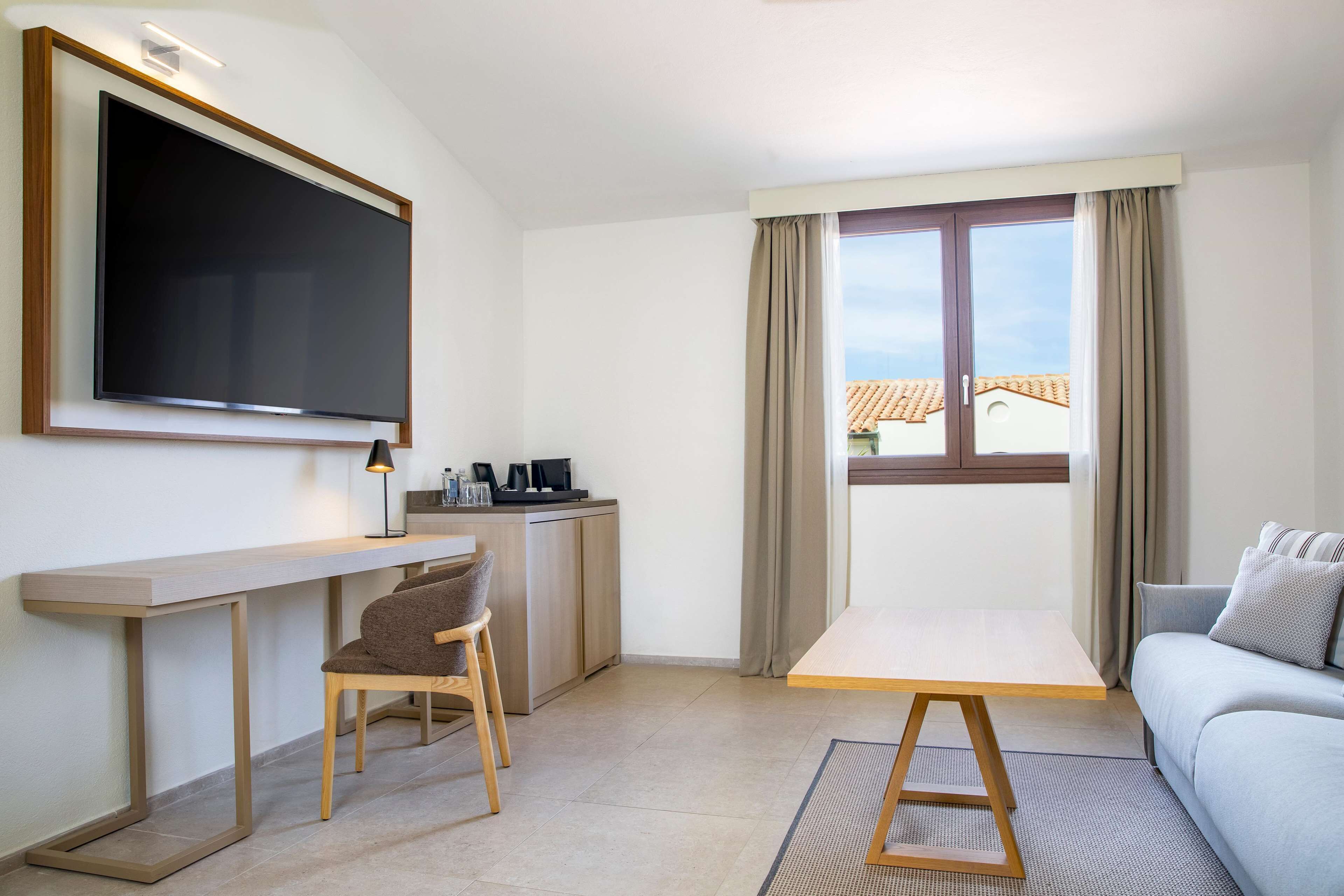 Une chambre d’hôtel moderne dotée d’une grande télévision à écran plat, d’un bureau en bois, d’un canapé confortable et d’une fenêtre offrant une vue sur les bâtiments.