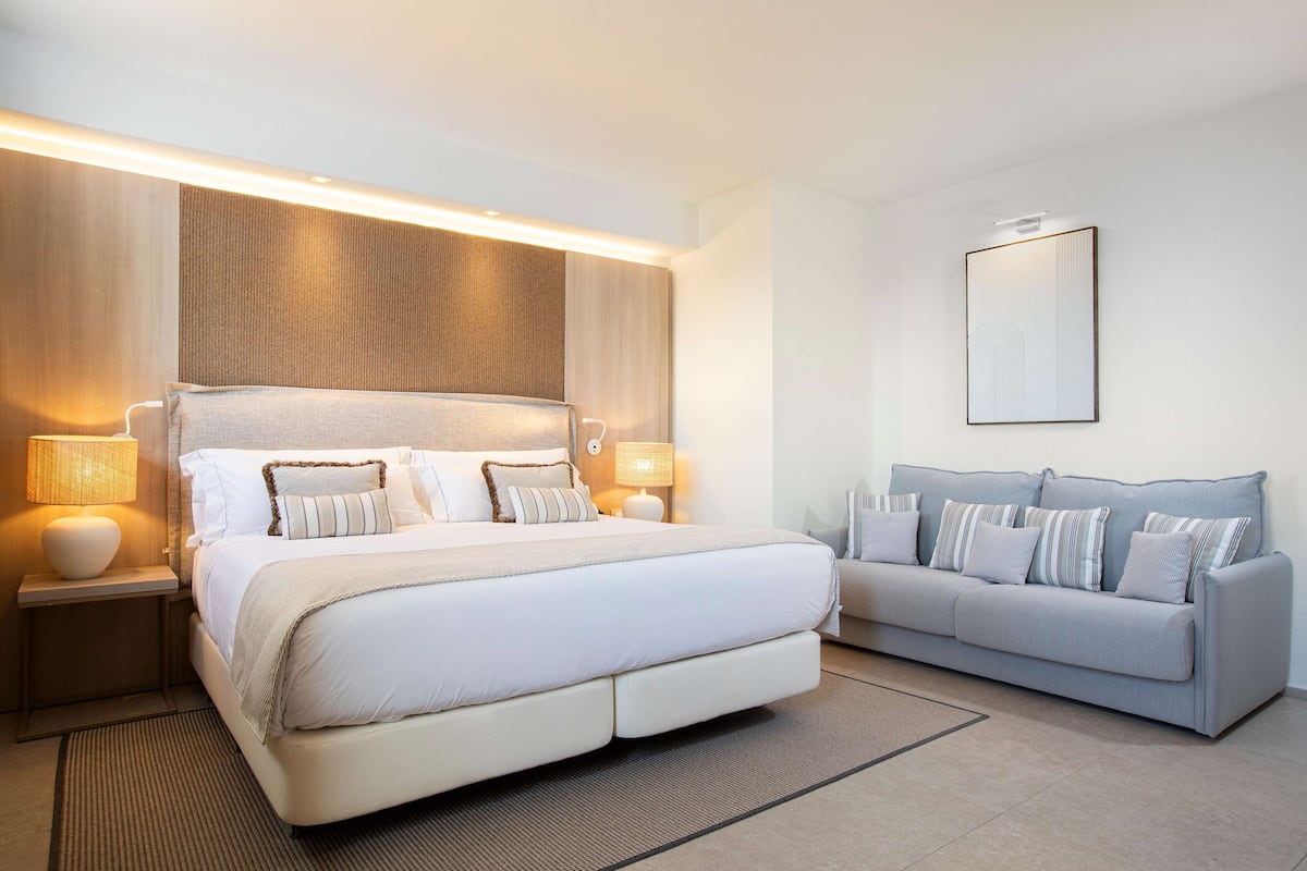 Un dormitorio moderno con una cama grande, un sofá y una mesita de noche con lámparas.