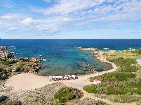 A coastal area with a sandy beach, a small white building, and a row of umbrellas. - Mangia's Santa Teresa Sardinia, Curio Collection by Hilton (Santa Teresa di Gallura)