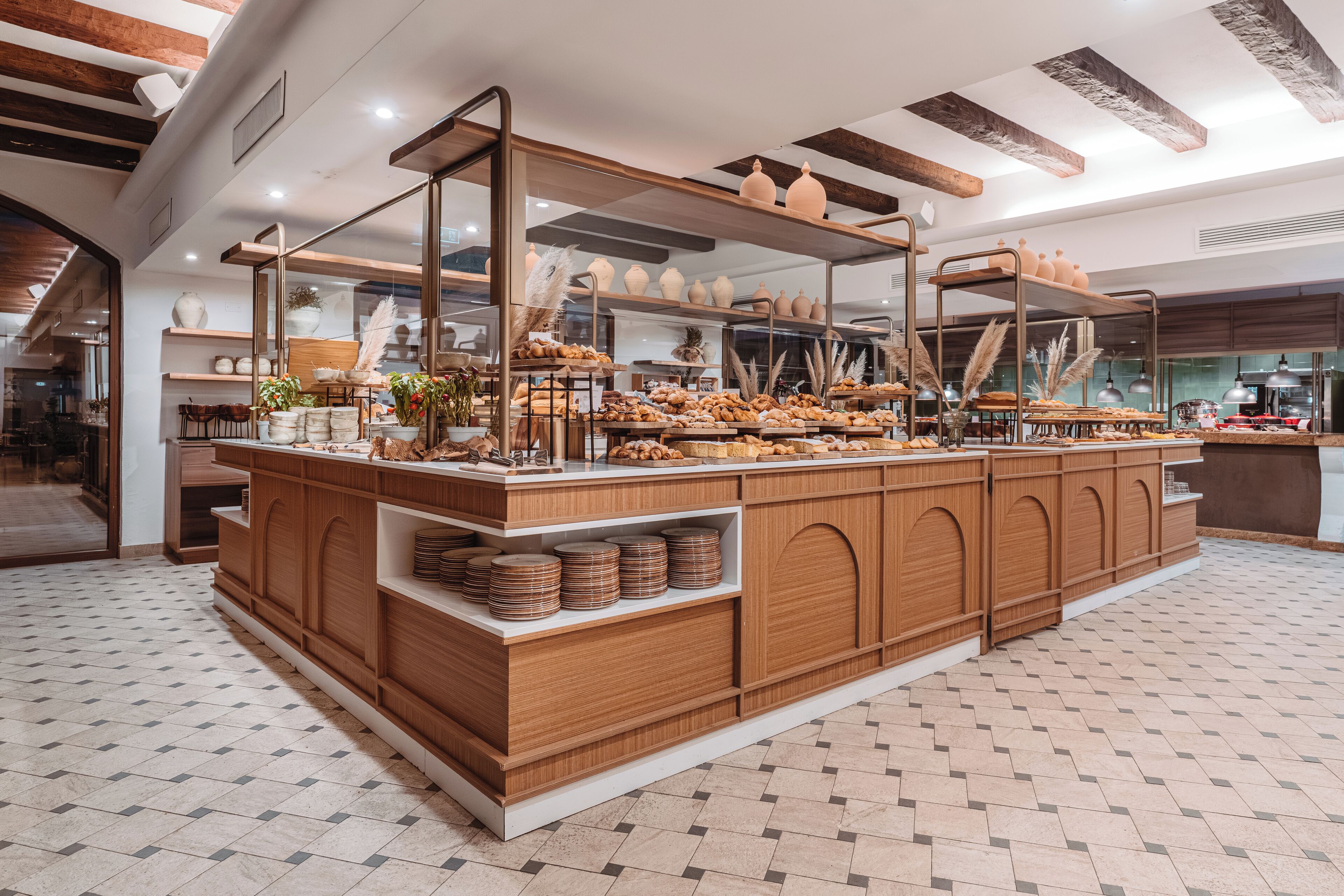 A bakery counter with pastries and bread, wooden shelves, and a tiled floor.
