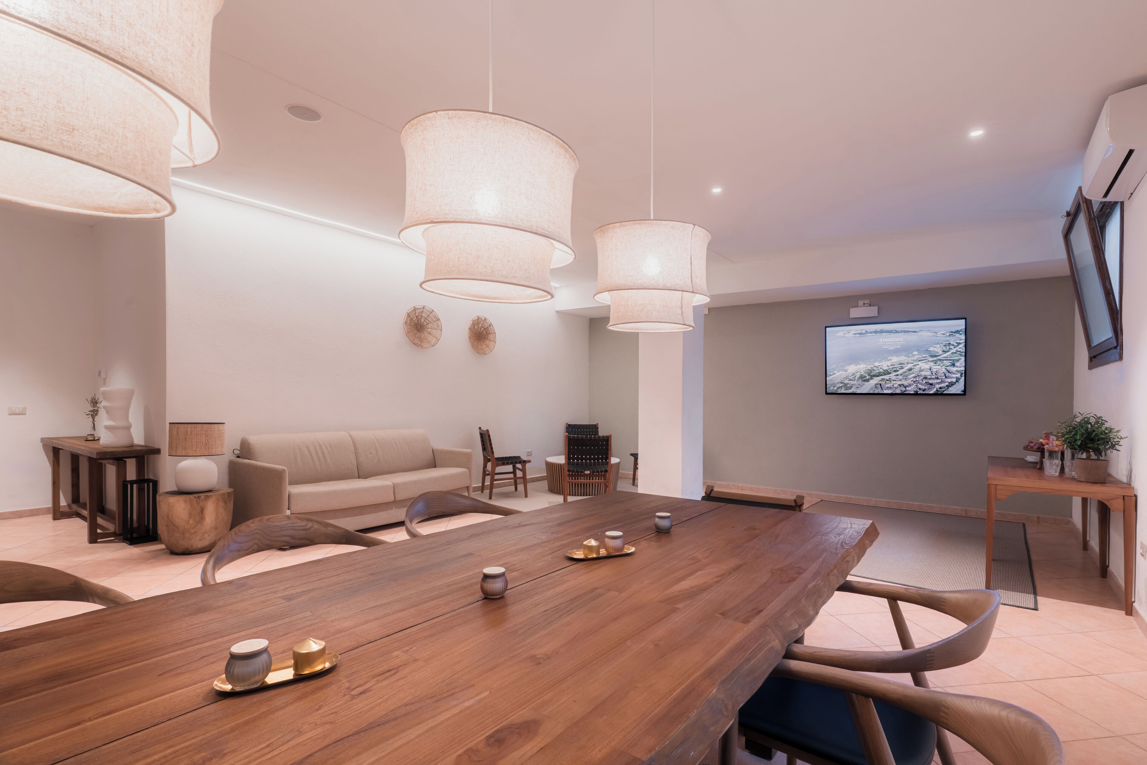 Una sala de estar moderna con una mesa de comedor de madera, un sofá beige y lámparas colgantes.