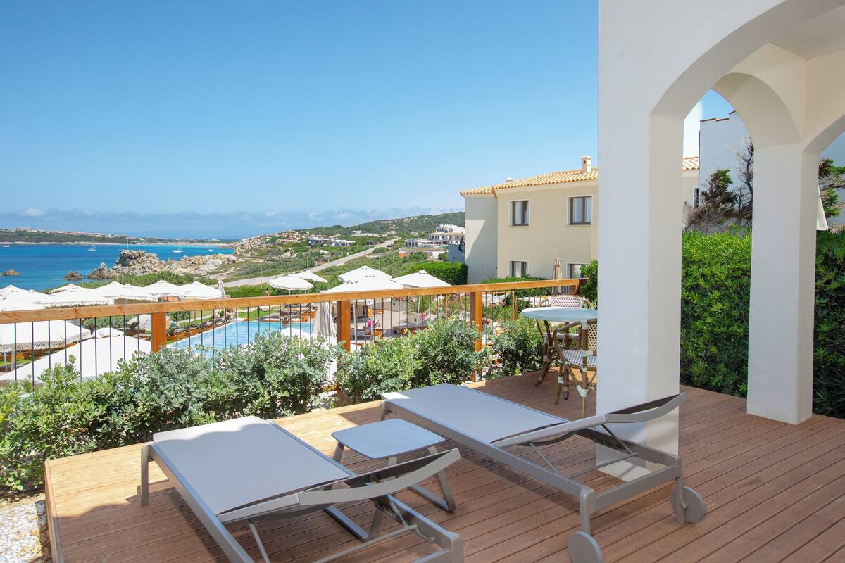 Terraza de madera con sillones de descanso con vista a una piscina y al mar.