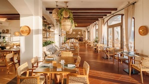 Ein geräumiges Restaurant mit Holztischen und -stühlen, hängenden Korbtreleuchtern und großen Fenstern für viel Tageslicht.