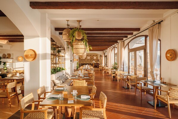 A spacious restaurant with wooden tables and chairs, hanging wicker chandeliers, and large windows allowing natural light. - Mangia's Santa Teresa Sardinia, Curio Collection by Hilton (Santa Teresa di Gallura)