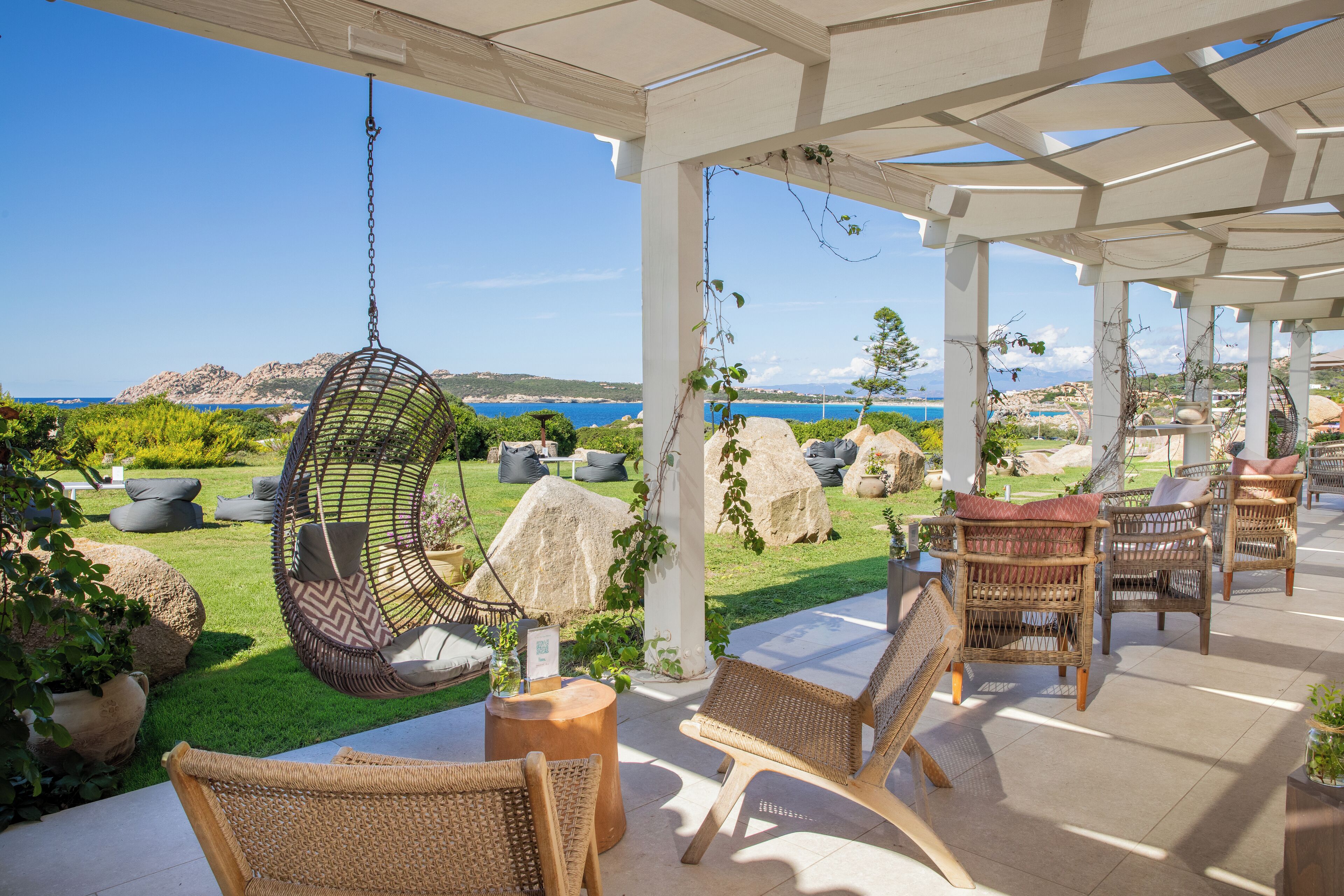 Un espacio de descanso al aire libre con mobiliario de mimbre, una silla colgante y vista al mar.