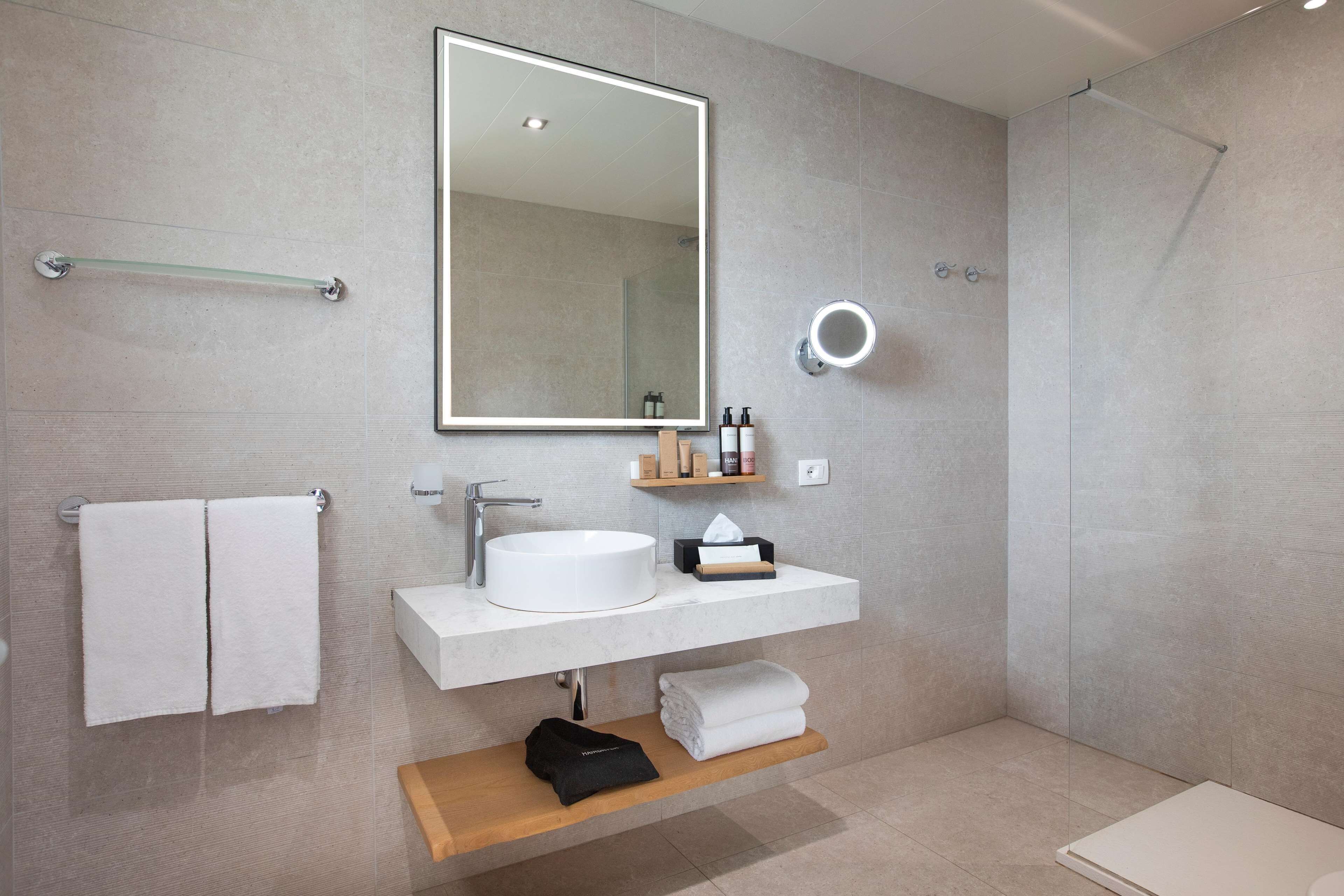 A modern bathroom with a large mirror, white sink, and a glass shower enclosure.