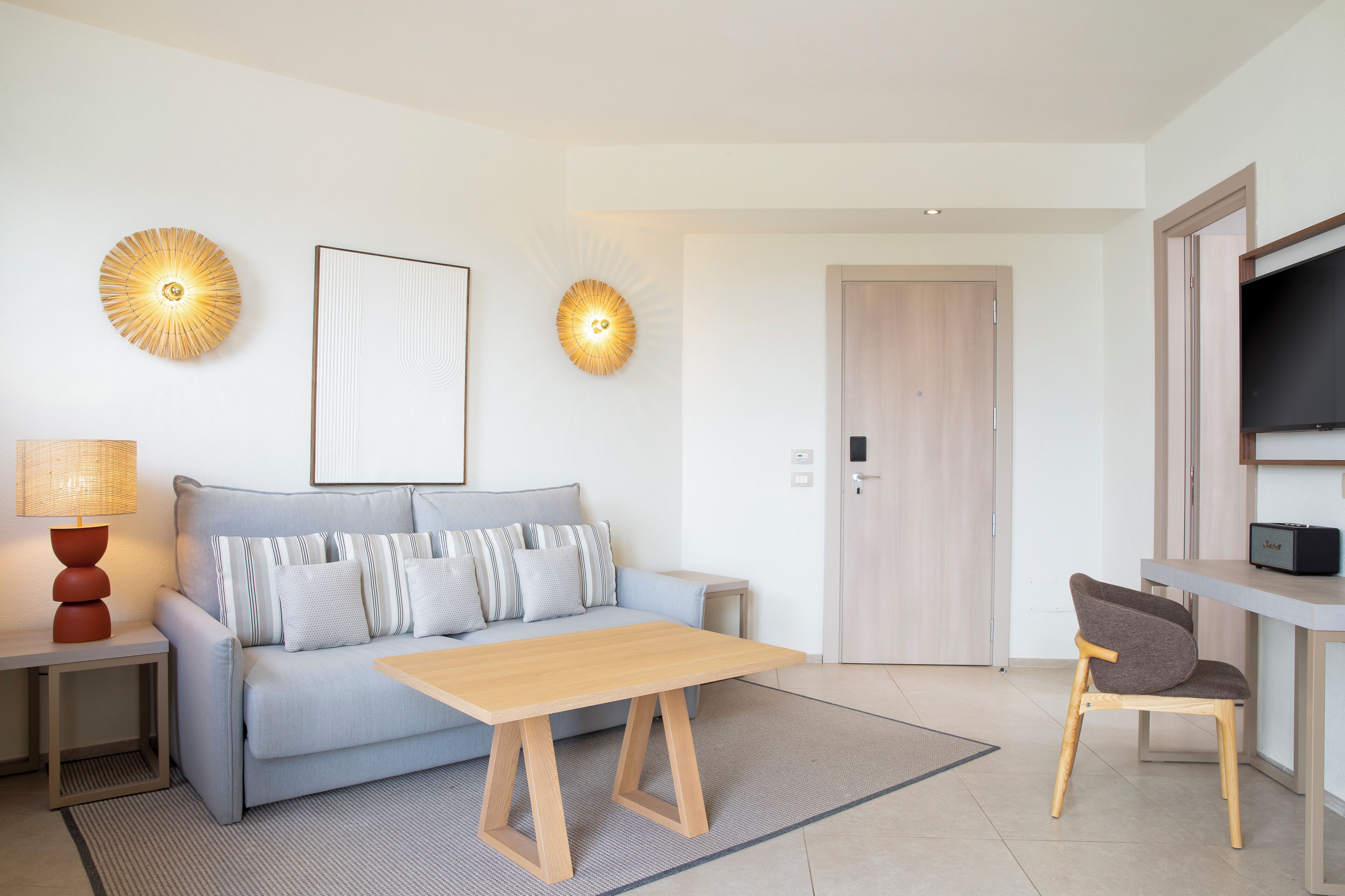Een moderne woonkamer met een bank, een houten salontafel, een bijzettafeltje met een lamp, en een tv op een meubel.