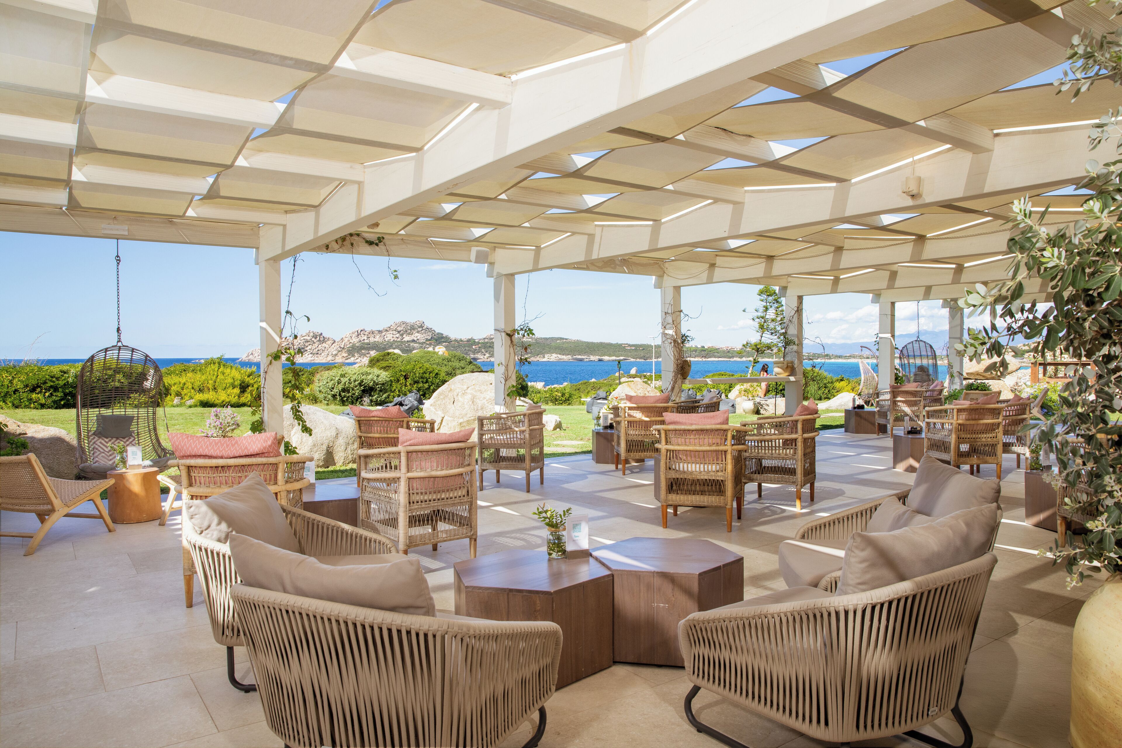 Une terrasse extérieure avec des meubles en osier, une vue sur la mer et une structure en forme de pergola.
