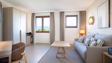 Une chambre d’hôtel moderne équipée d’un canapé, d’une table à manger, d’une chaise, d’une armoire et offrant une vue sur la mer.