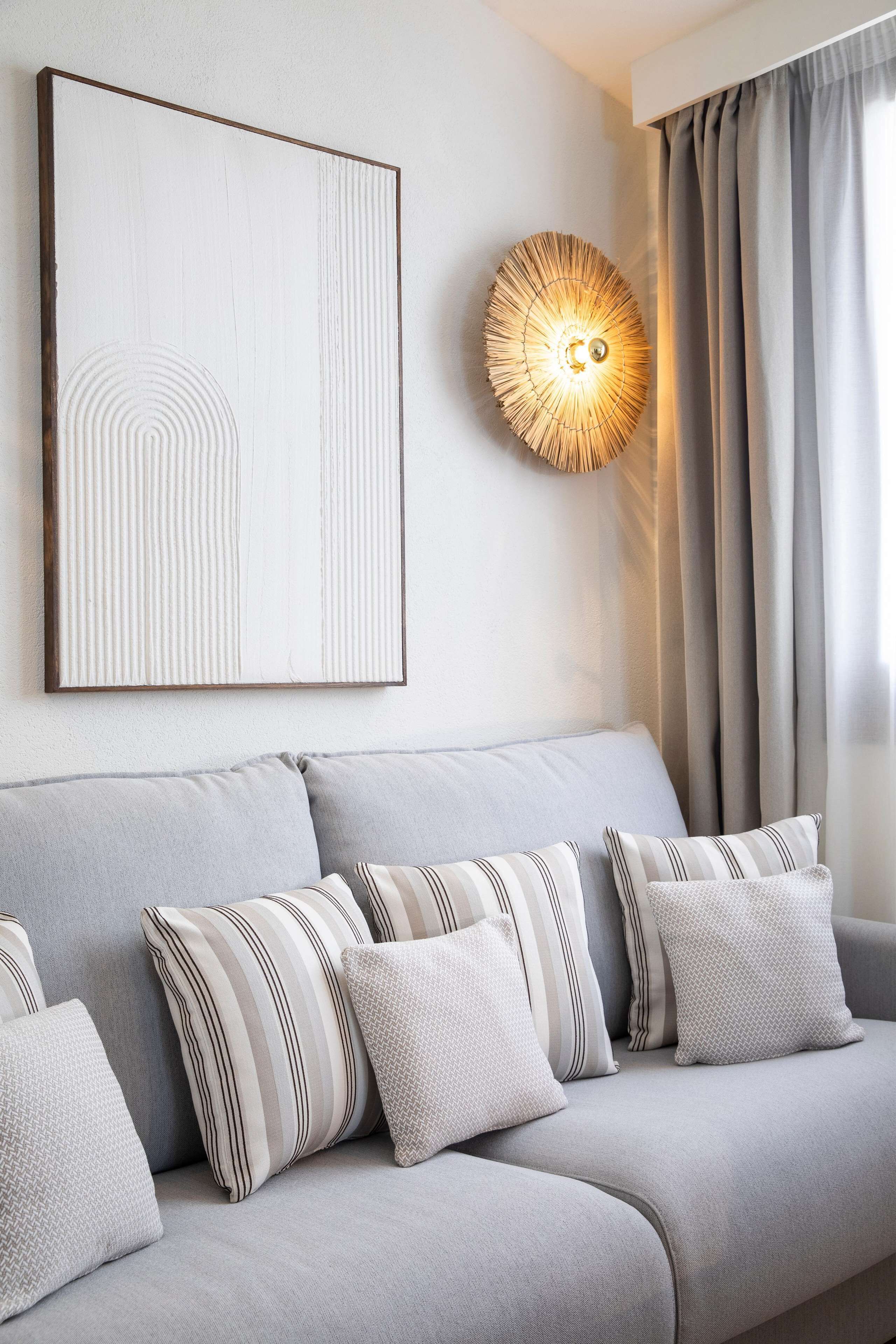 Una sala de estar moderna con un sofá gris, almohadas a rayas y con textura, un cuadro abstracto colgado en la pared y una lámpara decorativa en la pared.