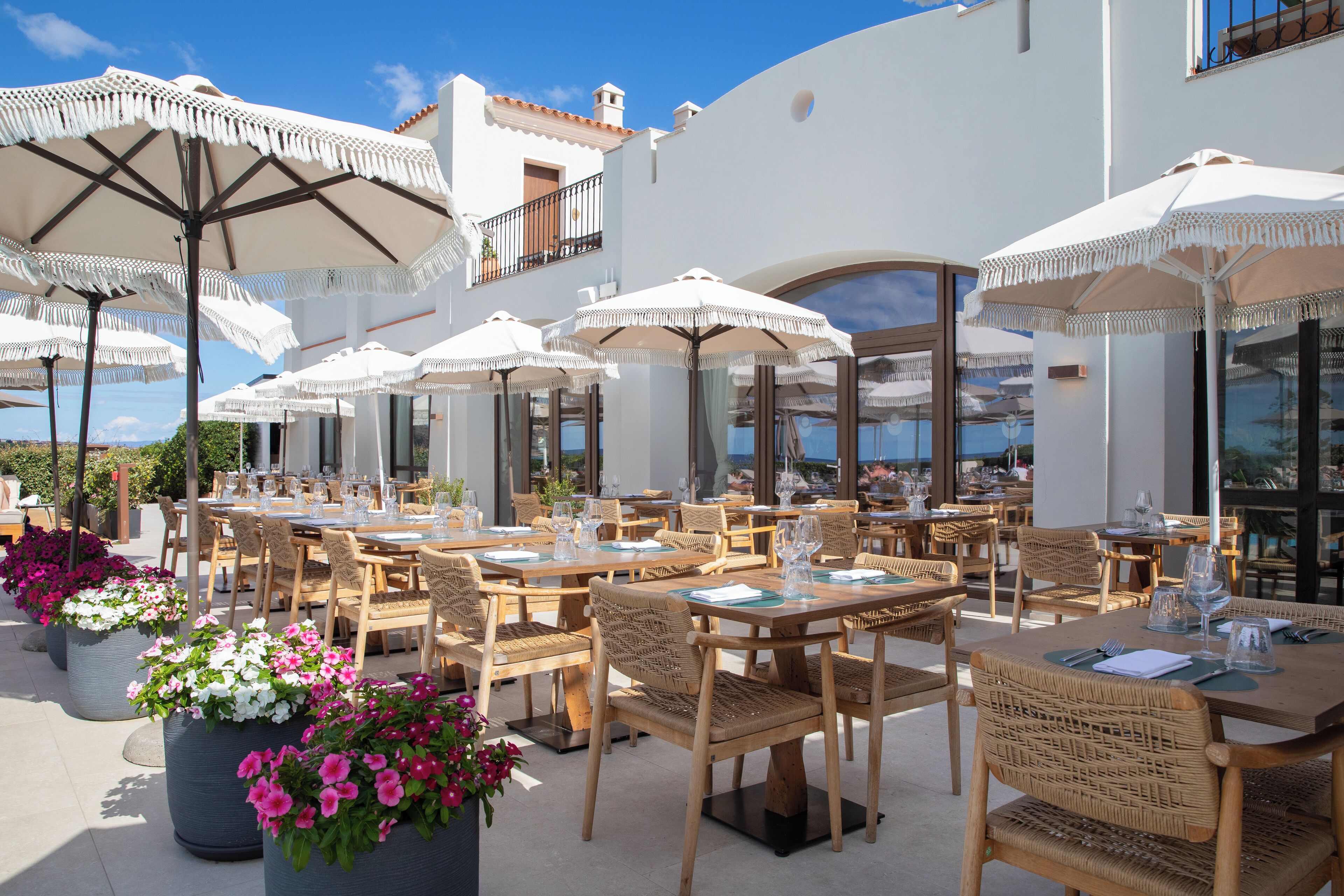 An outdoor dining area with multiple tables and chairs, surrounded by large umbrellas.