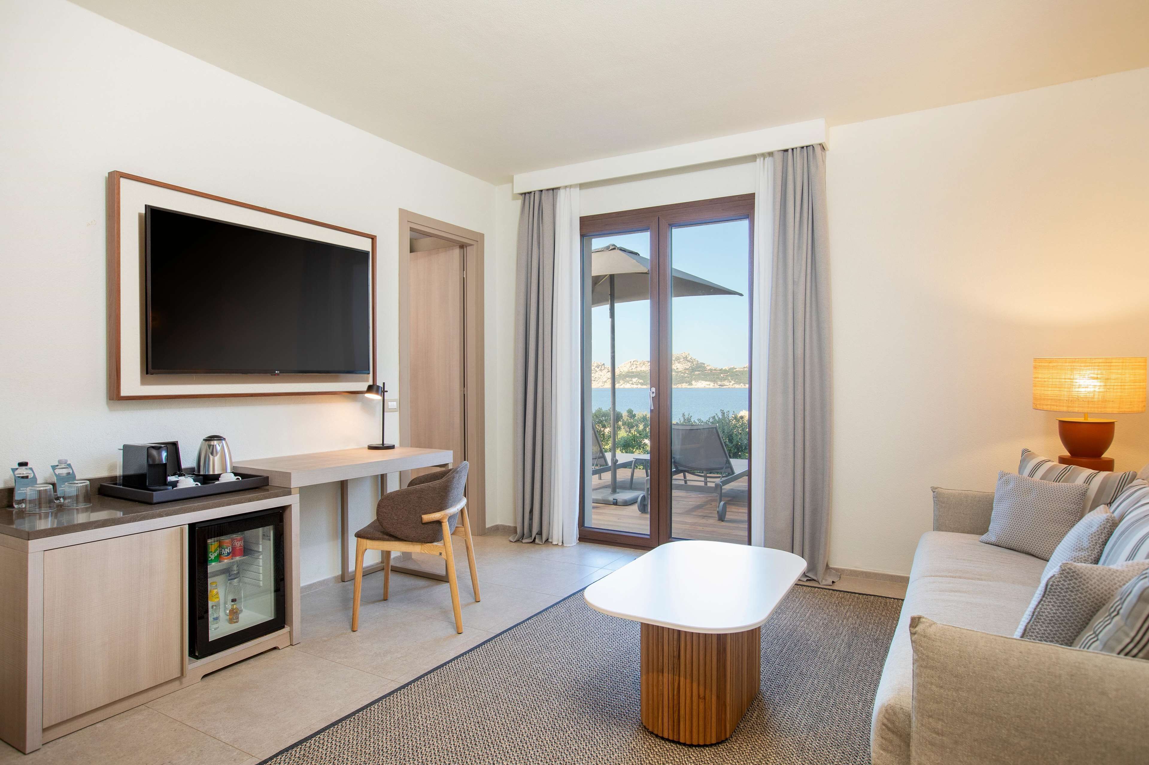 Habitación de hotel moderna con televisión de pantalla plana, una kitchenette pequeña, zona de comedor, sofá y vistas al exterior.