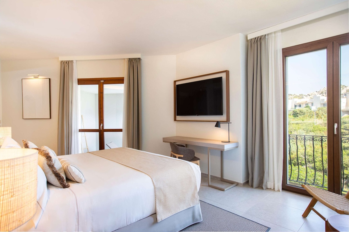 Ein Hotelzimmer mit Bett, Schreibtisch, Fernseher und einem Balkon mit Aussicht.