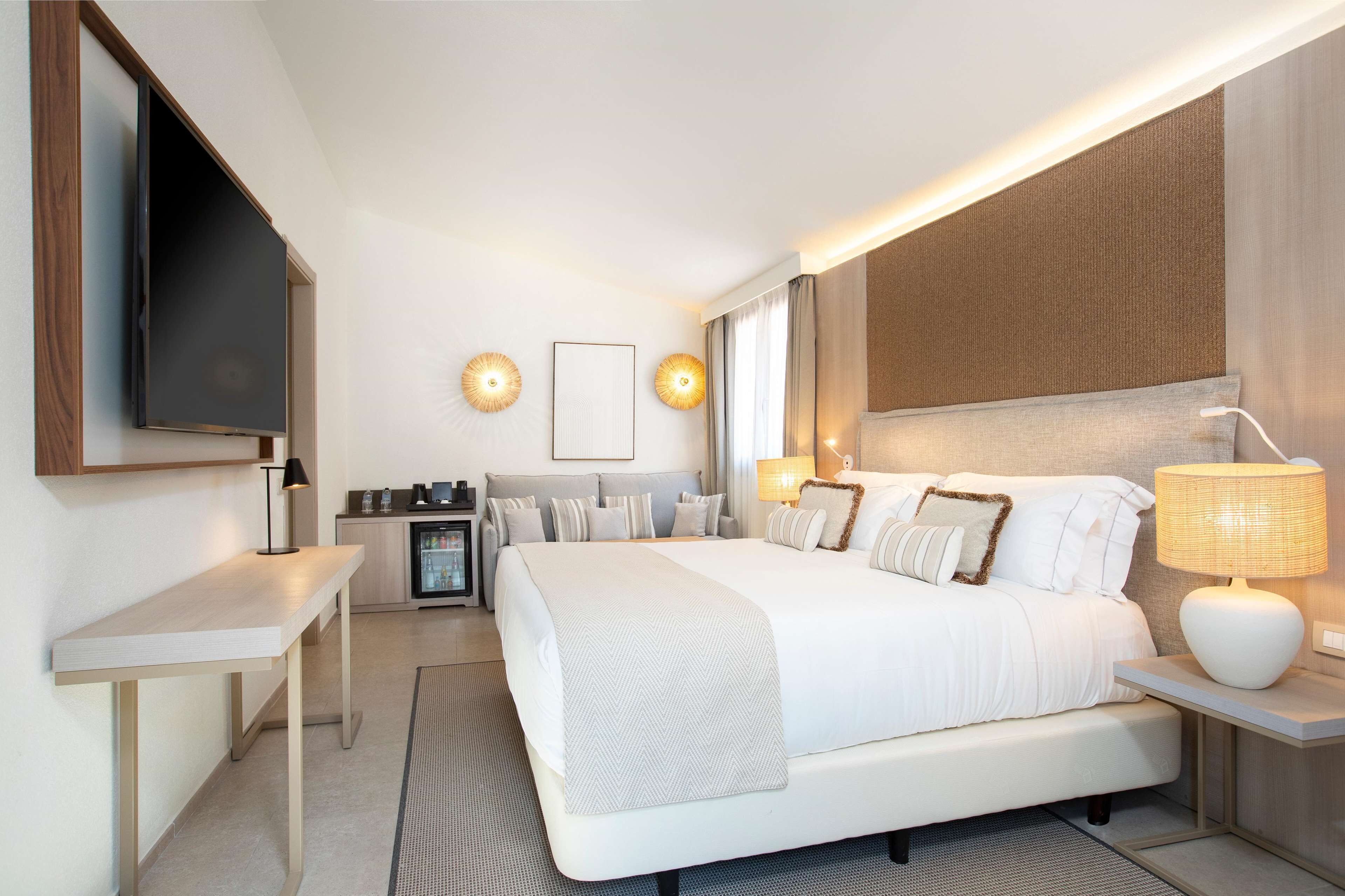 Una habitación de hotel moderna con una cama grande, mesitas de noche, un televisor de pantalla plana y un minibar.