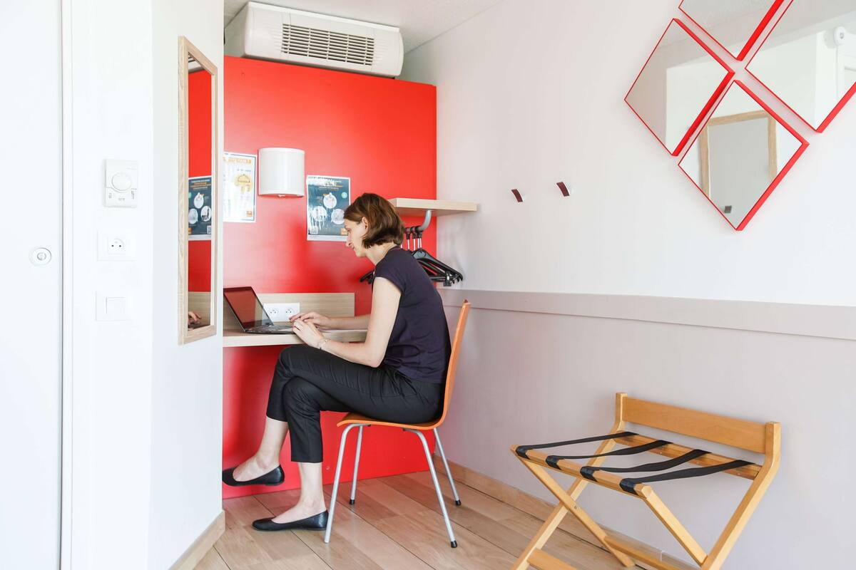 Une pièce avec un mur d’accent rouge, un bureau avec un ordinateur portable, une chaise et un banc en bois.