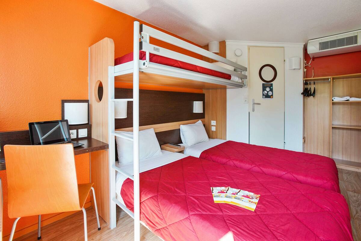 Une chambre avec un lit superposé, un bureau et une chaise, une armoire et une porte ornée d’un motif circulaire.