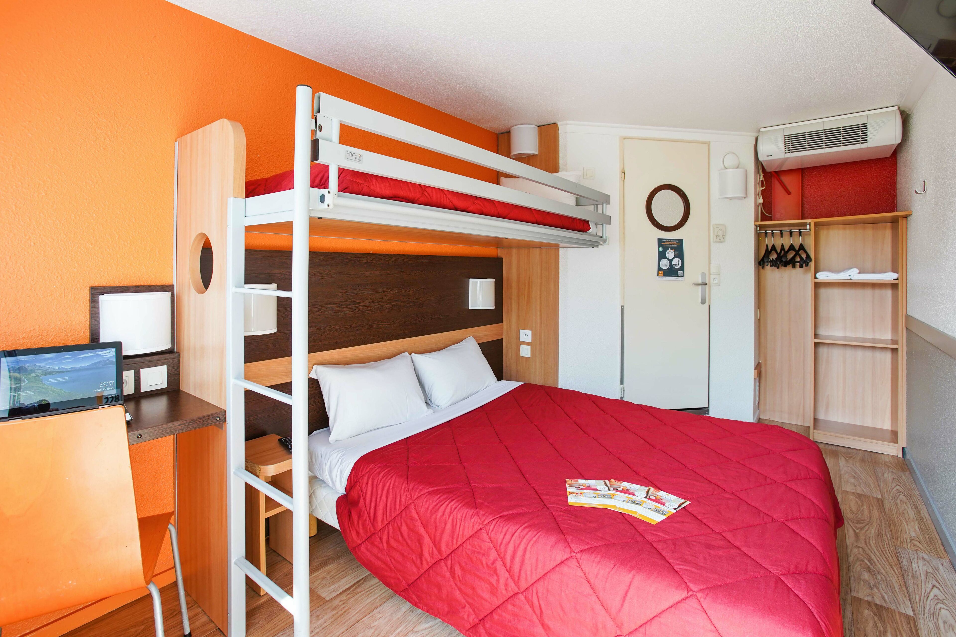 A bunk bed room with a desk, a wardrobe, and a small seating area.
