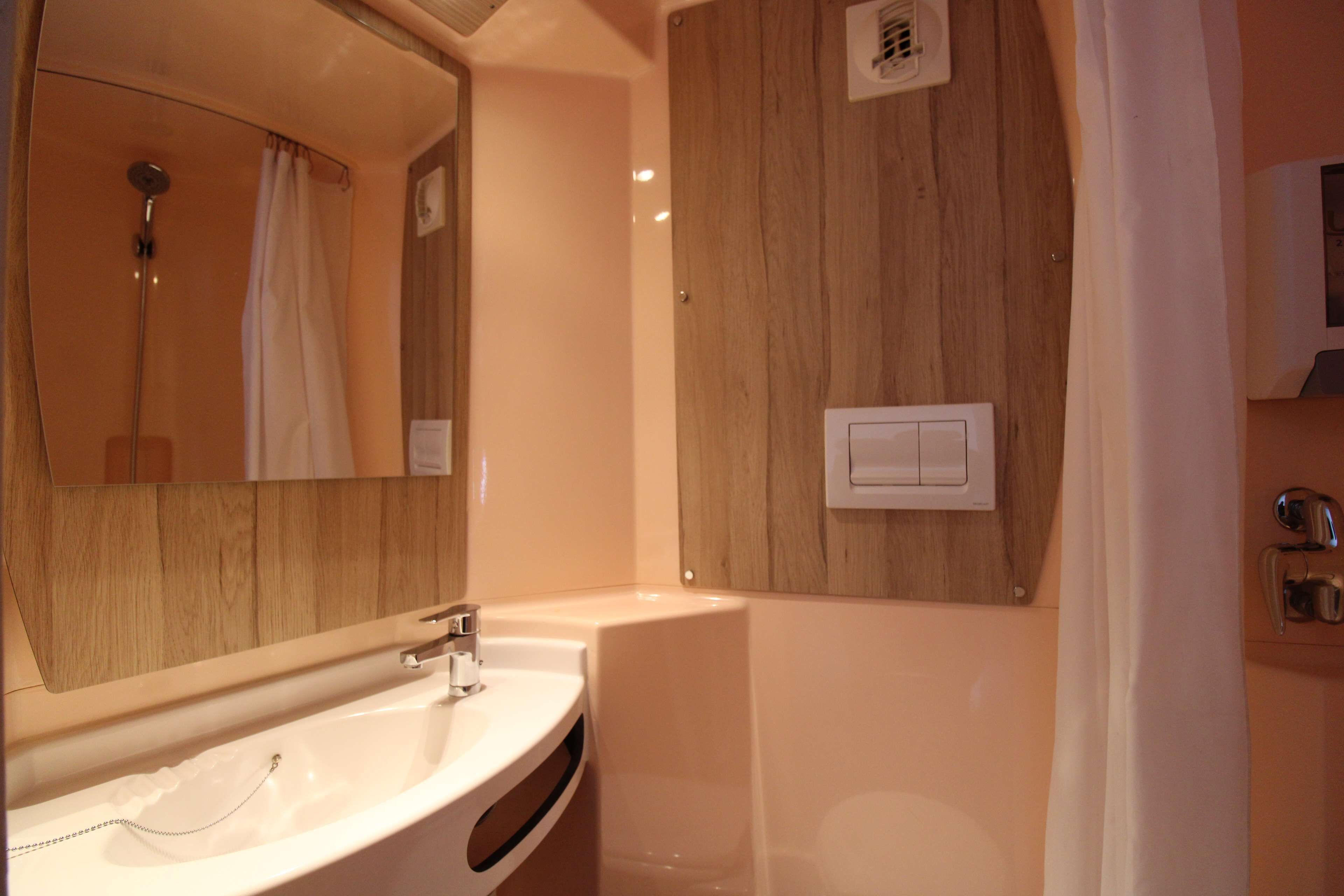 A bathroom with a sink, mirror, shower, and wooden panel wall.