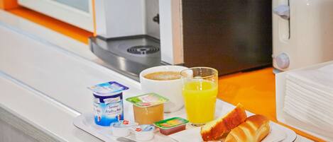 Bandeja de desayuno con yogur, una taza de café, un vaso de zumo de naranja y cruasanes sobre una mesa de habitación de hotel.