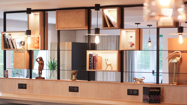 A modern reception desk with a wooden finish, multiple shelves with books and decorative items, and pendant lighting. - Hôtel Premiere Classe Melun Senart - Vert Saint Denis (Vert-Saint-Denis)