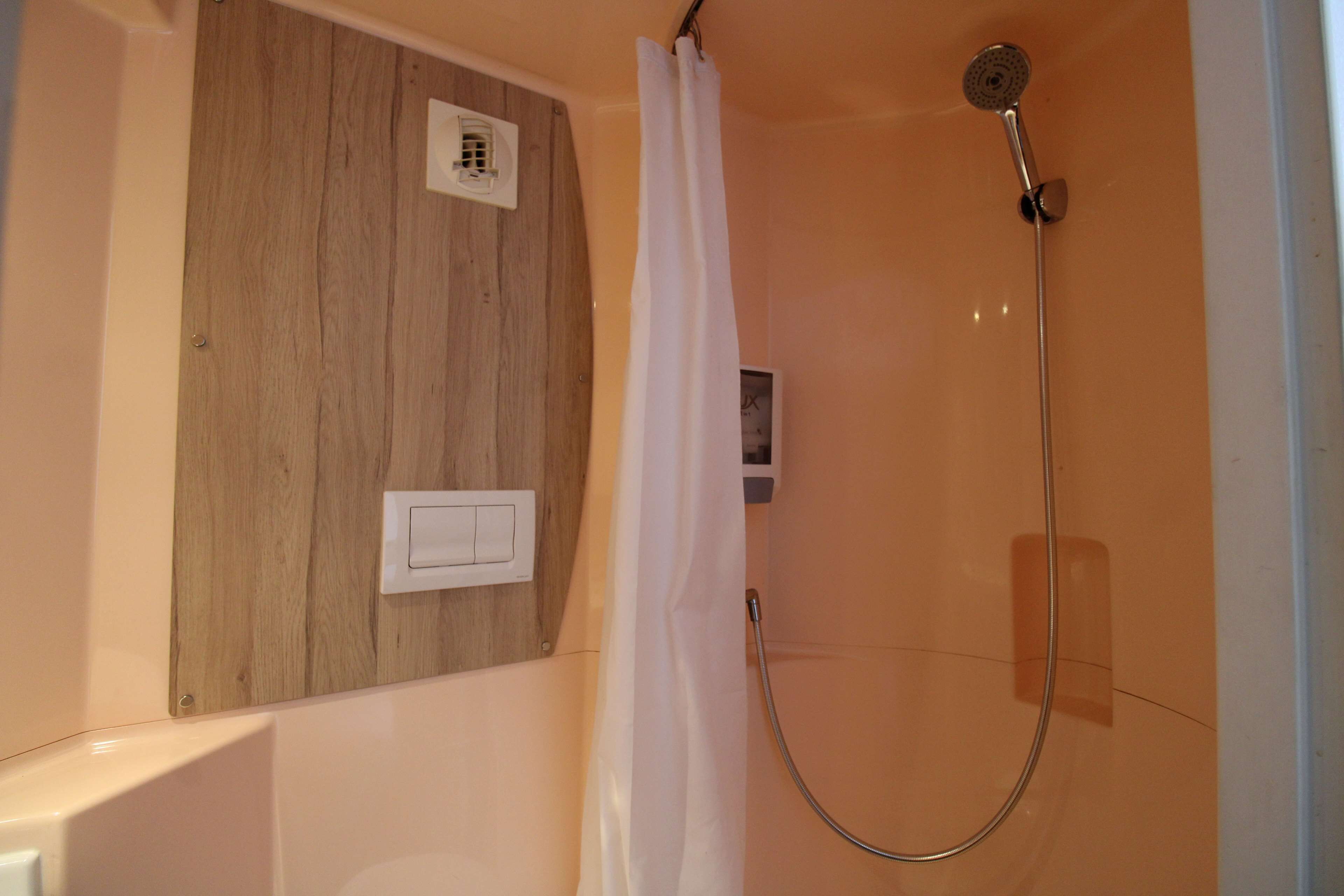 A shower area with a wooden panel, a white curtain, and a handheld showerhead.