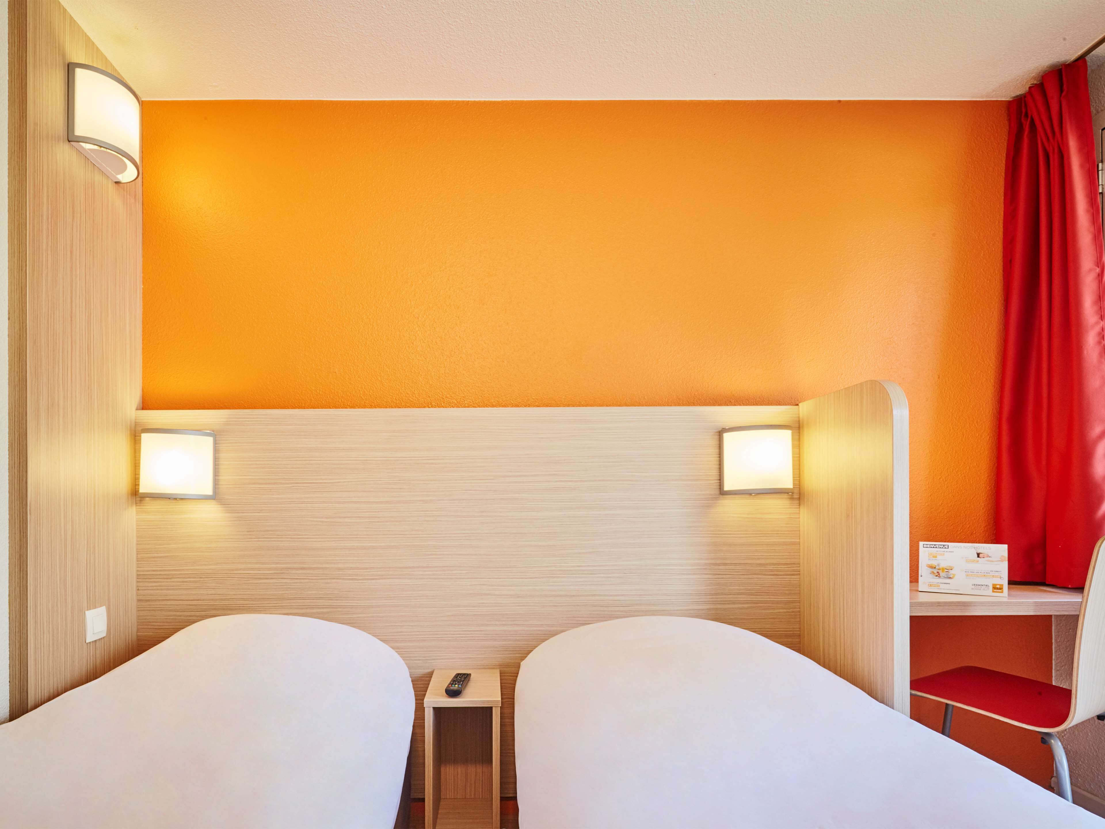 A hotel room with two beds, a small table, a chair, and a red curtain.