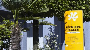 Un letrero amarillo con texto blanco y un símbolo de flor blanca, que indica un hotel llamado "Premiere Classe" con traducciones en varios idiomas.